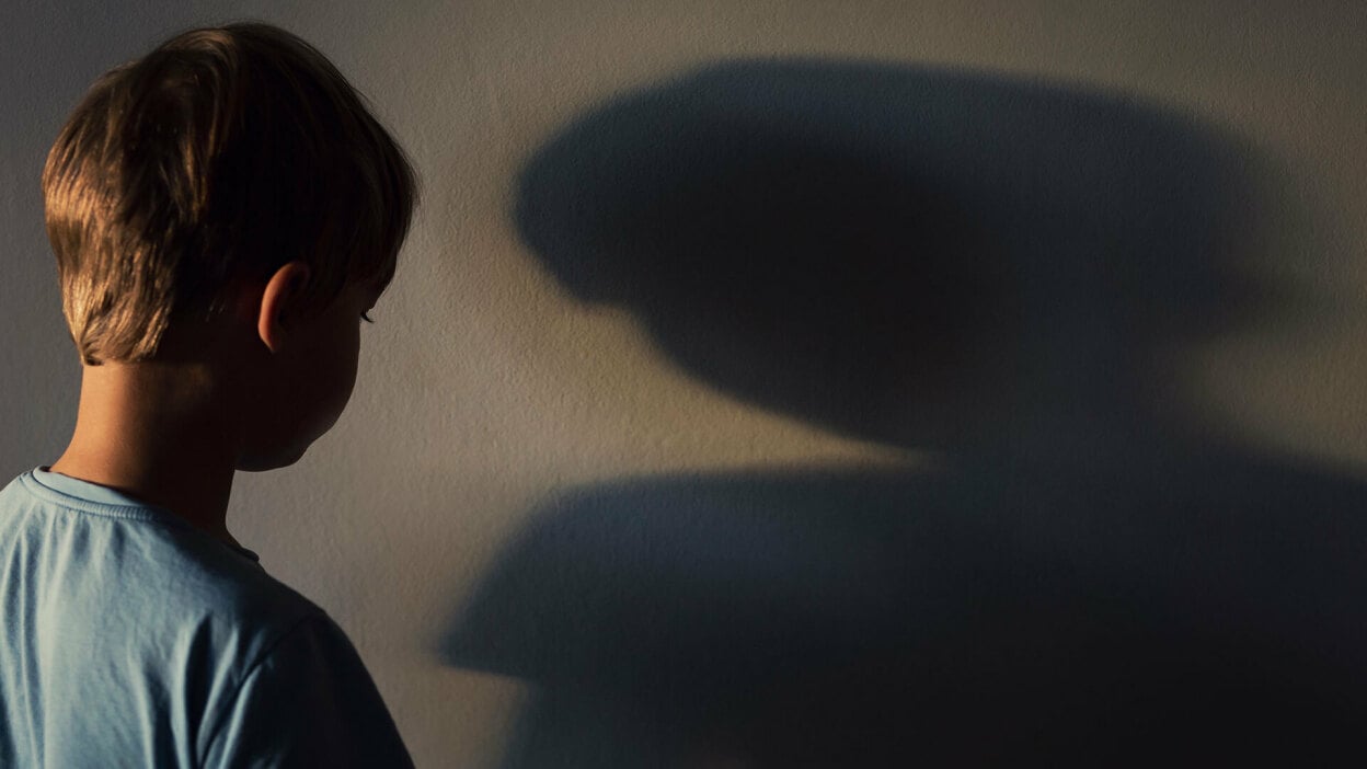 A boy looks at his shadow on a wall.