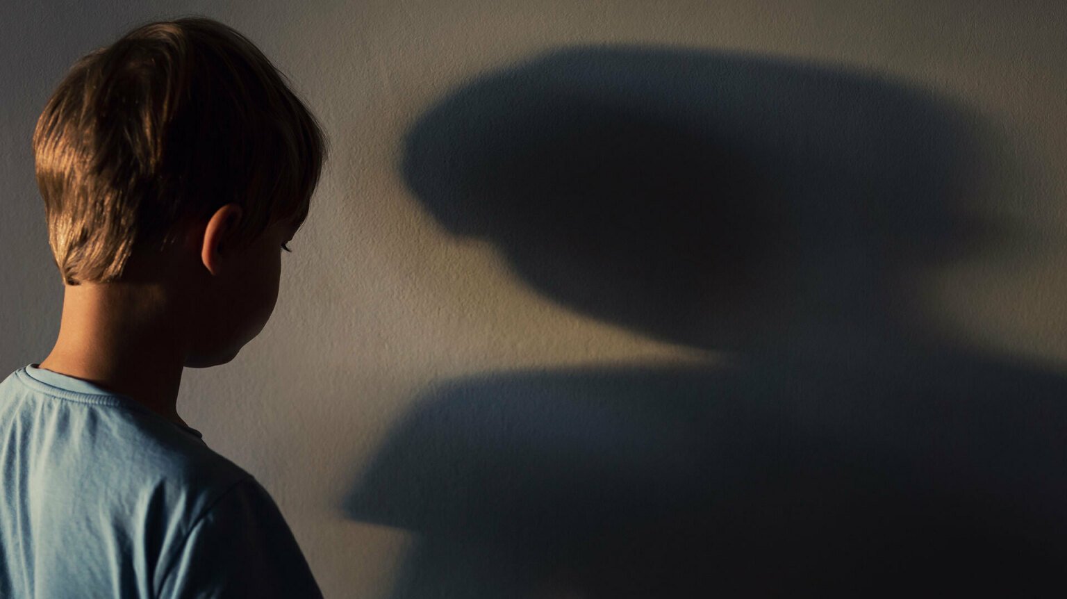A boy looks at his shadow on a wall.