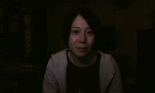 A woman in a dark room looks at the camera.
