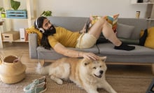 Person wearing headphones laying on couch while petting dog on floor