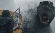 Godzilla roars down at a woman standing by a school bus.