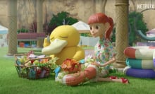 In a stop-motion Pokemon TV series, Psyduck sits with a girl on a green lawn with baskets of flowers.