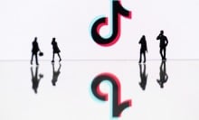 The TikTok logo framed by the shadows of four people. 
