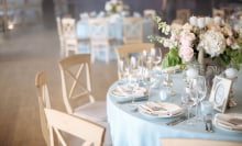 An empty table at a wedding, served with cutlery, flowers and crockery and covered with a tablecloth. 