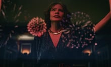 A stylish woman stands leaning on a wall as fireworks explode in the background.