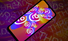 A phone screen displaying overlapping rainbow threads logos on a faded background reading, "threads" over and over again.