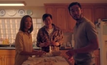 A mother and her two grown sons stand around the kitchen.