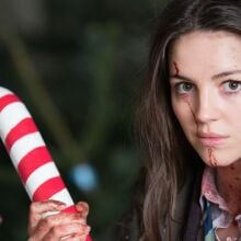 A blood-spattered Anna, played by Ella Hunt, holds a large candy cane weapon.