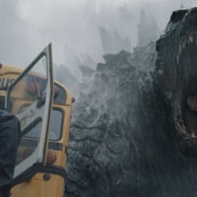 Godzilla roars down at a woman standing by a school bus.