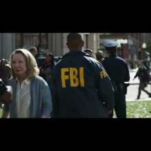 A man in an FBI jacket walks through a crowd.