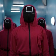 A group of Squid Game guards in pink jumpsuits and masks with shapes on them.