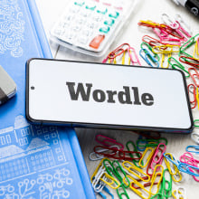 A Wordle logo seen displayed on a smartphone against a cluttered desk.
