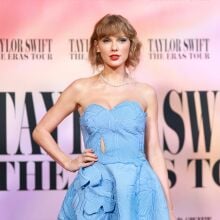 Taylor Swift posing on The Eras Tour Movie premiere red carpet in a light blue floral dress.
