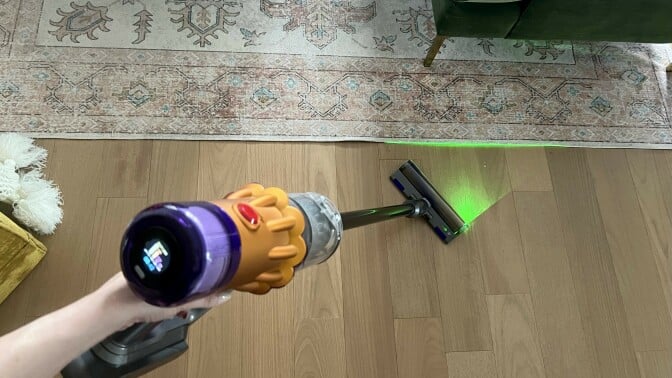 Person holding Dyson V12 Detect Slim to clean hardwood floor with laser on