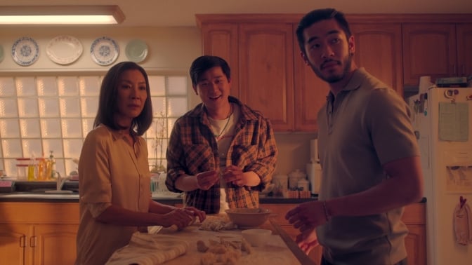 A mother and her two grown sons stand around the kitchen.