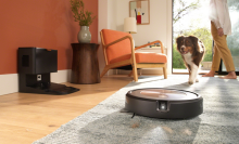 Roomba with headlight cleaning carpet with dog and person's feet in background
