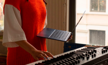 a close-up of a woman playing a piano with one hand while holding an apple macbook air in the other