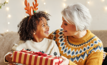 Happy afro american curly boy sitting on grandmother lap with christmas present, smiling at camera