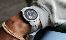 The Garmin Instinct 2S watch in a light grey color on someone's wrist, which also has a few bracelets on it