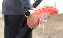Running stretching - runner wearing smartwatch. Closeup of running shoes, woman stretching leg as warm-up before run with sport activity tracker watch at wrist to monitor the heart rate during cardio.