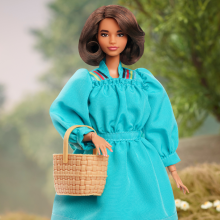 A barbie with short brown hair stands in a long turquoise dress holding a woven basket.