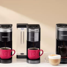 Three Keurig coffee makers on countertop with coffee pods and plant in background
