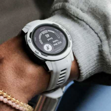The Garmin Instinct 2S watch in a light grey color on someone's wrist, which also has a few bracelets on it