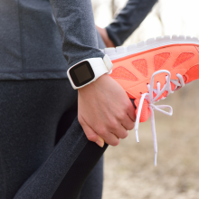 Running stretching - runner wearing smartwatch. Closeup of running shoes, woman stretching leg as warm-up before run with sport activity tracker watch at wrist to monitor the heart rate during cardio.