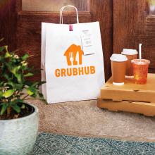 a food delivery order from Grubhub sits on a front door that includes pizza boxes, drinks, and a brown paper bag