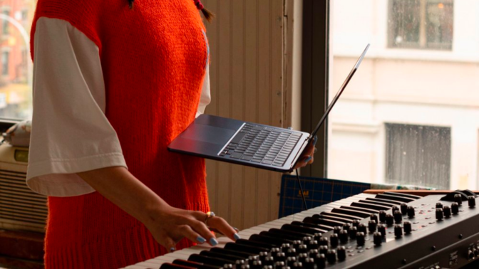 a close-up of a woman playing a piano with one hand while holding an apple macbook air in the other